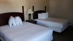 Ein Hotelzimmer mit zwei Betten, jeweils mit weißer Bettwäsche und Kissen, einem Nachttisch mit Lampe und einem dunklen Holz-Kopfteil.