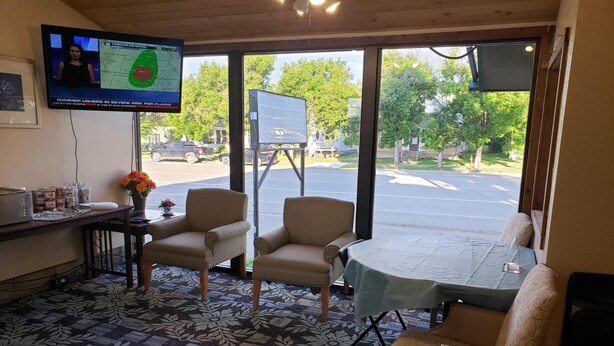 Ein Zimmer mit einem großen Fenster, einem Fernseher, der eine Wettervorhersage zeigt, einem Tisch mit einer Tischdecke und zwei Stühlen.