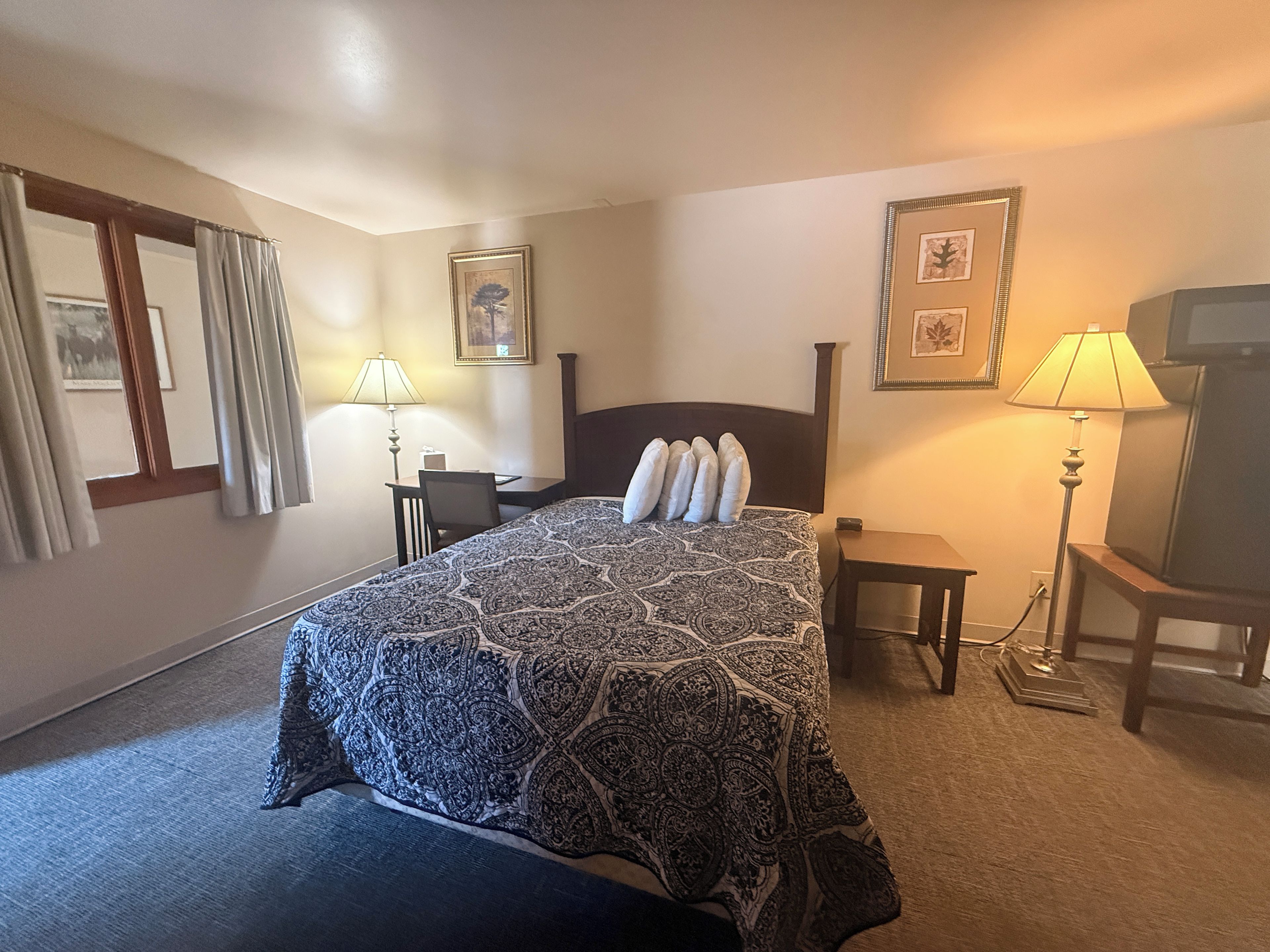 Una habitación de hotel con una cama, un escritorio, dos lámparas y cuadros en las paredes.