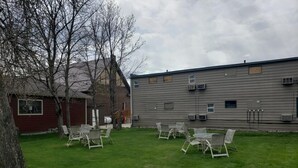 Ein Garten mit Rasenfläche, mehreren Stühlen und einem Gebäude mit Klimaanlagen.