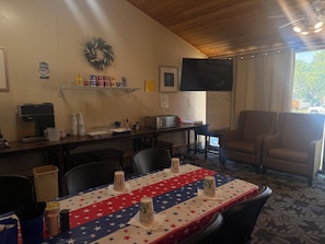 Zona de menjador amb taula preparada per a dues persones, una màquina de cafè i un quadre de menú.