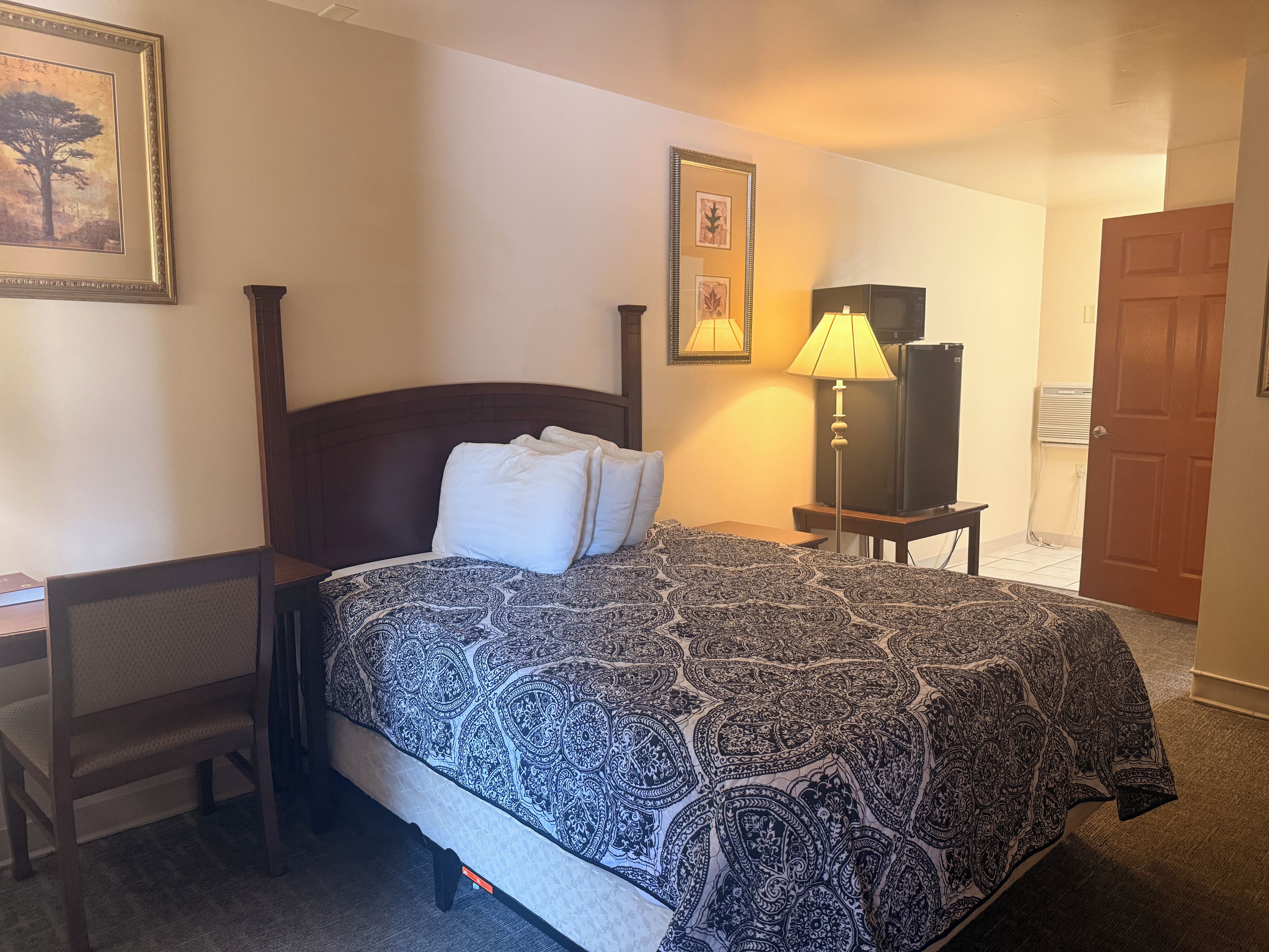 A hotel room with a bed, a nightstand, a lamp, a television, and a door.