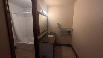 A bathroom with a shower, sink, mirror, and a wall-mounted heater.