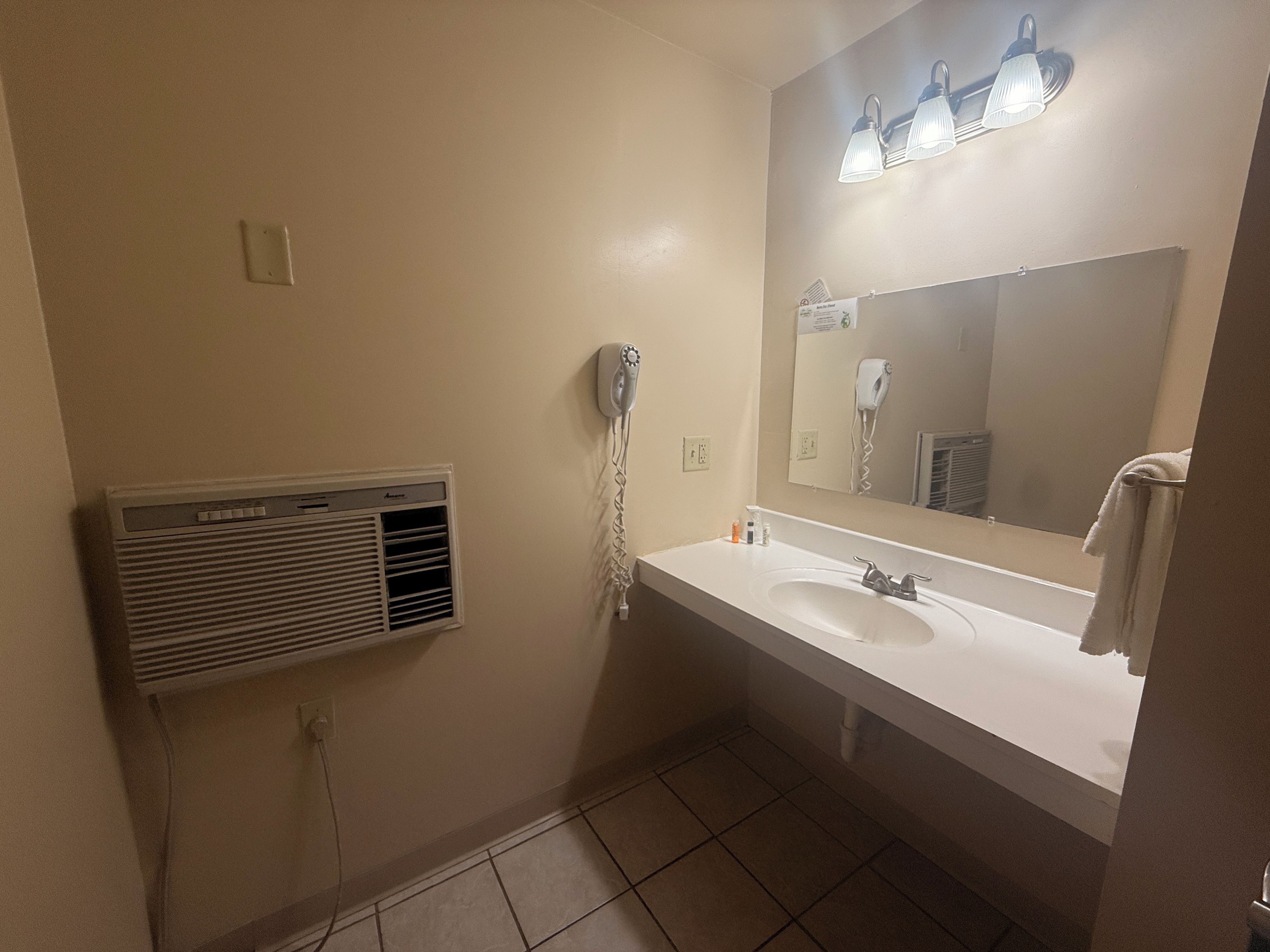 Un baño con lavamanos blanco, un espejo con luces, un secador de pelo y un calentador de pared.