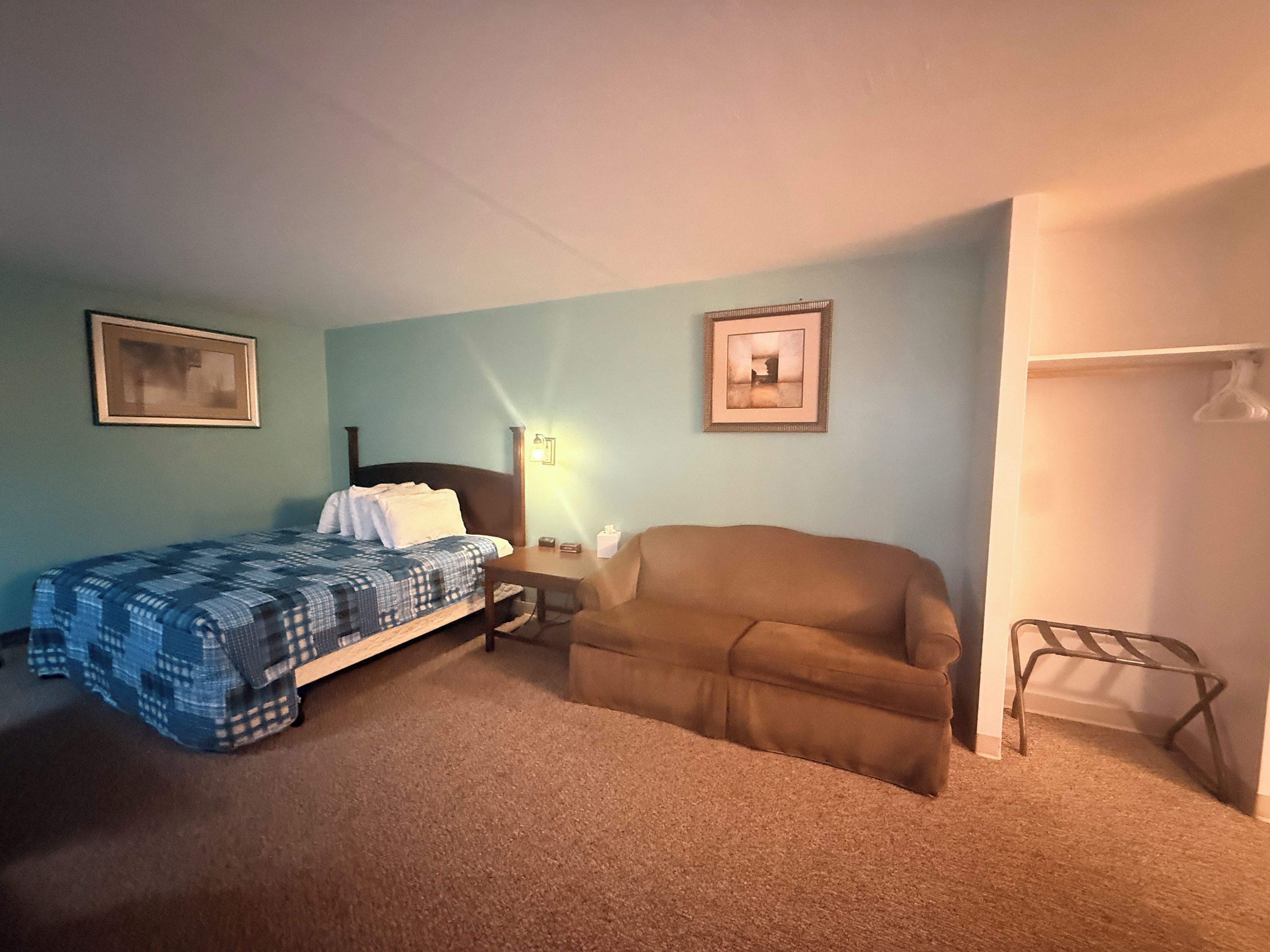Una camera da letto con un letto, una sedia, un comodino e due quadri appesi al muro.
