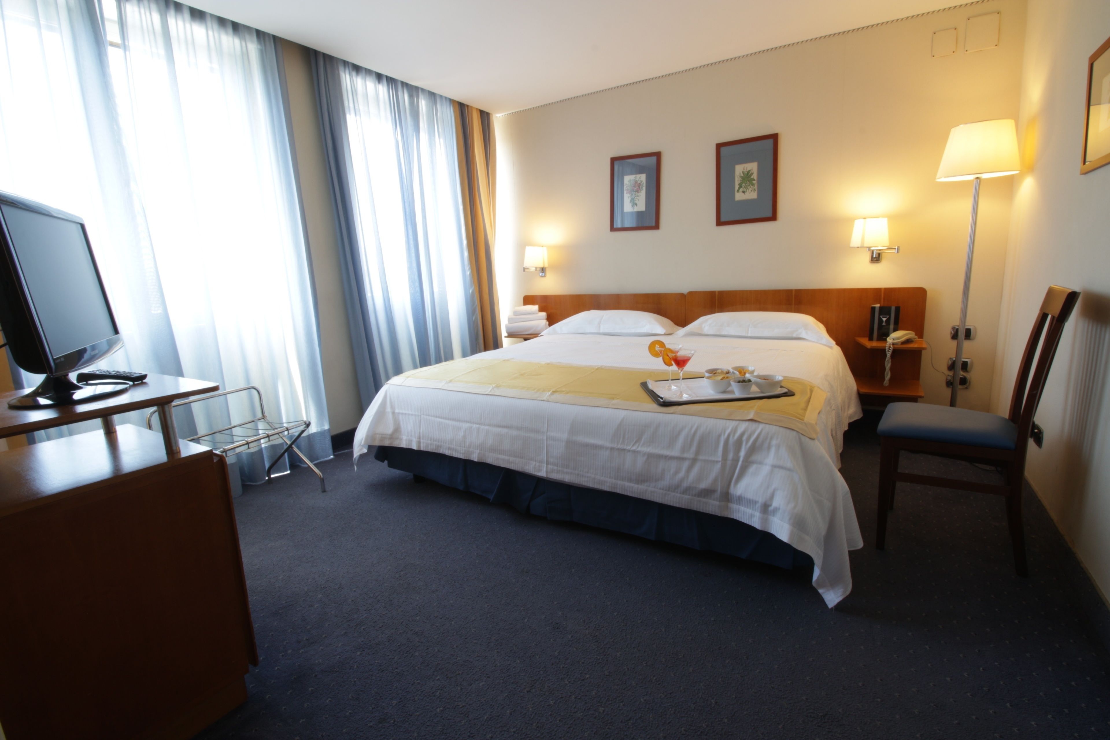 A hotel room with a bed, bedside tables, a desk, a chair, and a television.