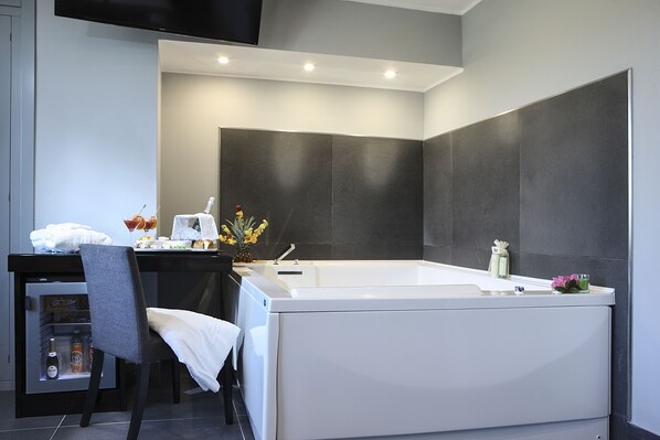 A modern bathroom with a bathtub, a vanity with a mirror, and a chair. - Best Western JFK Hotel (Naples)