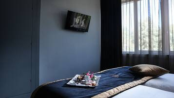 Habitació d'hotel amb un llit, un televisor fixat a la paret i una finestra amb cortines.