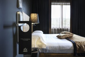 A hotel room with a bed, a lamp, and a door with a handle. - Best Western JFK Hotel (Naples)