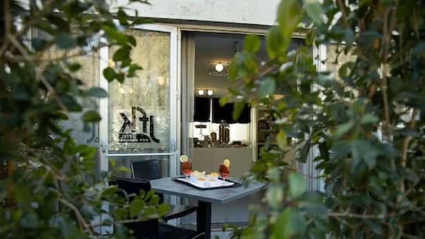 A dining area with a table set for two, a window with a view of the interior, and greenery in the foreground. - Best Western JFK Hotel (Naples)