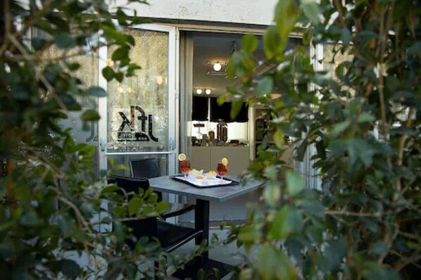 Ein Essbereich mit einem Tisch für zwei Personen, einem Fenster mit Blick ins Innere und Grünpflanzen im Vordergrund.