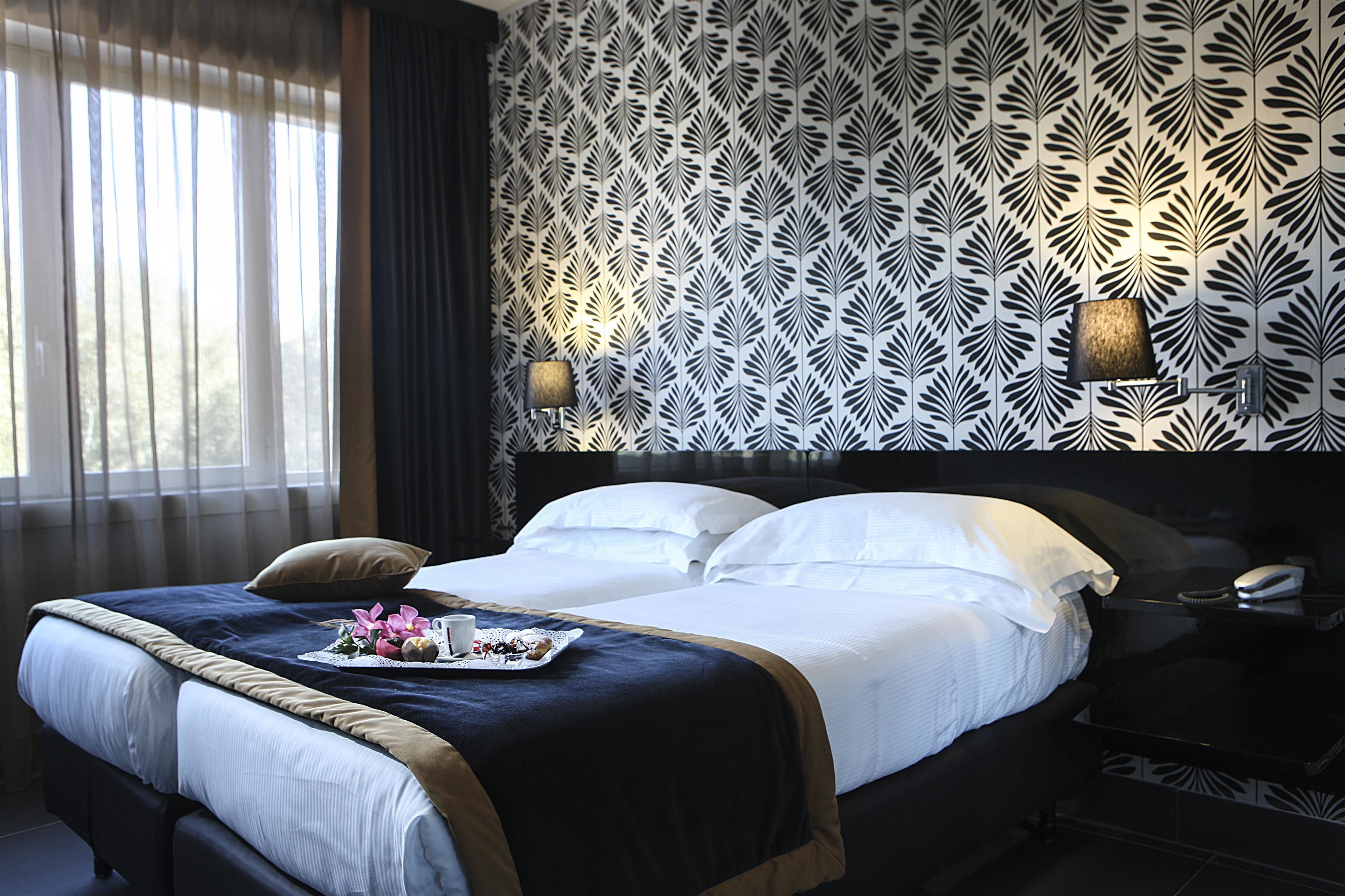 A neatly made bed with a tray of flowers and a cup, a dark headboard, and patterned wallpaper.