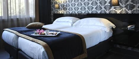 A neatly made bed with a tray of flowers and a cup, a dark headboard, and patterned wallpaper.