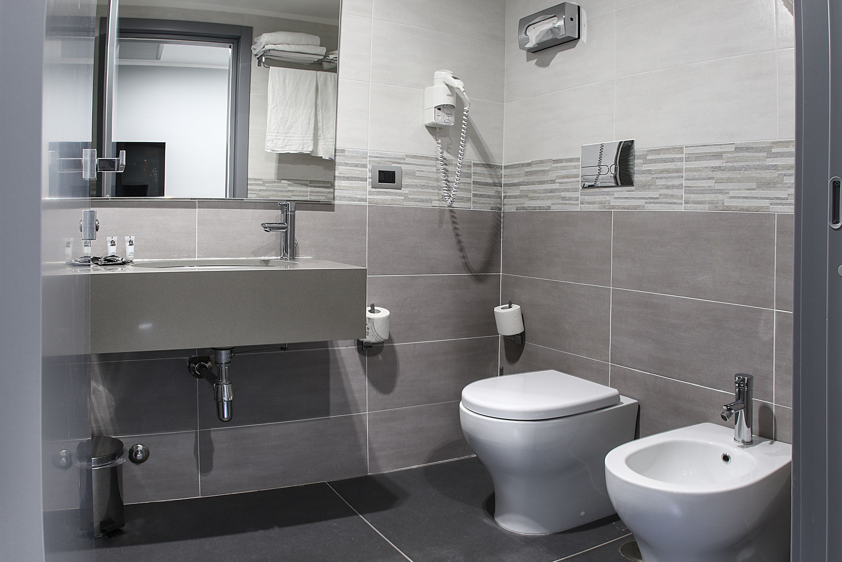 Egy modern fürőszoba mosdókagylóval, WC-vel, bidével és tükörrel.