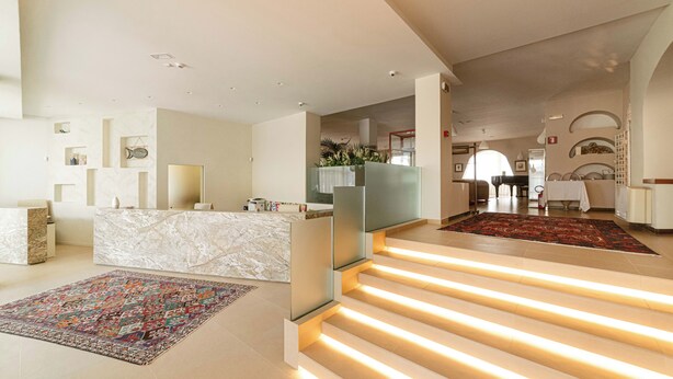 Un moderno vestíbulo de hotel con recepción de mármol, una alfombra colorida y una escalera con iluminación integrada.