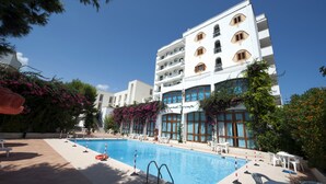 Un hotel con piscina, mobiliario exterior y un edificio blanco con balcones.