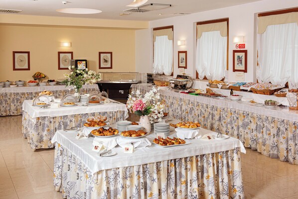 Montaje de bufé con varias mesas cubiertas con manteles blancos, que exhibe una variedad de alimentos y un centro de mesa floral.