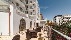 Una terraza en la azotea con mobiliario exterior, plantas en macetas y vistas de los edificios circundantes.