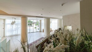 Un amplio hall de hotel con ventanas grandes, una columna central y un mostrador de recepción.