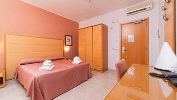 A hotel room with a bed, a desk, a chair, a wardrobe, and an air conditioning unit.