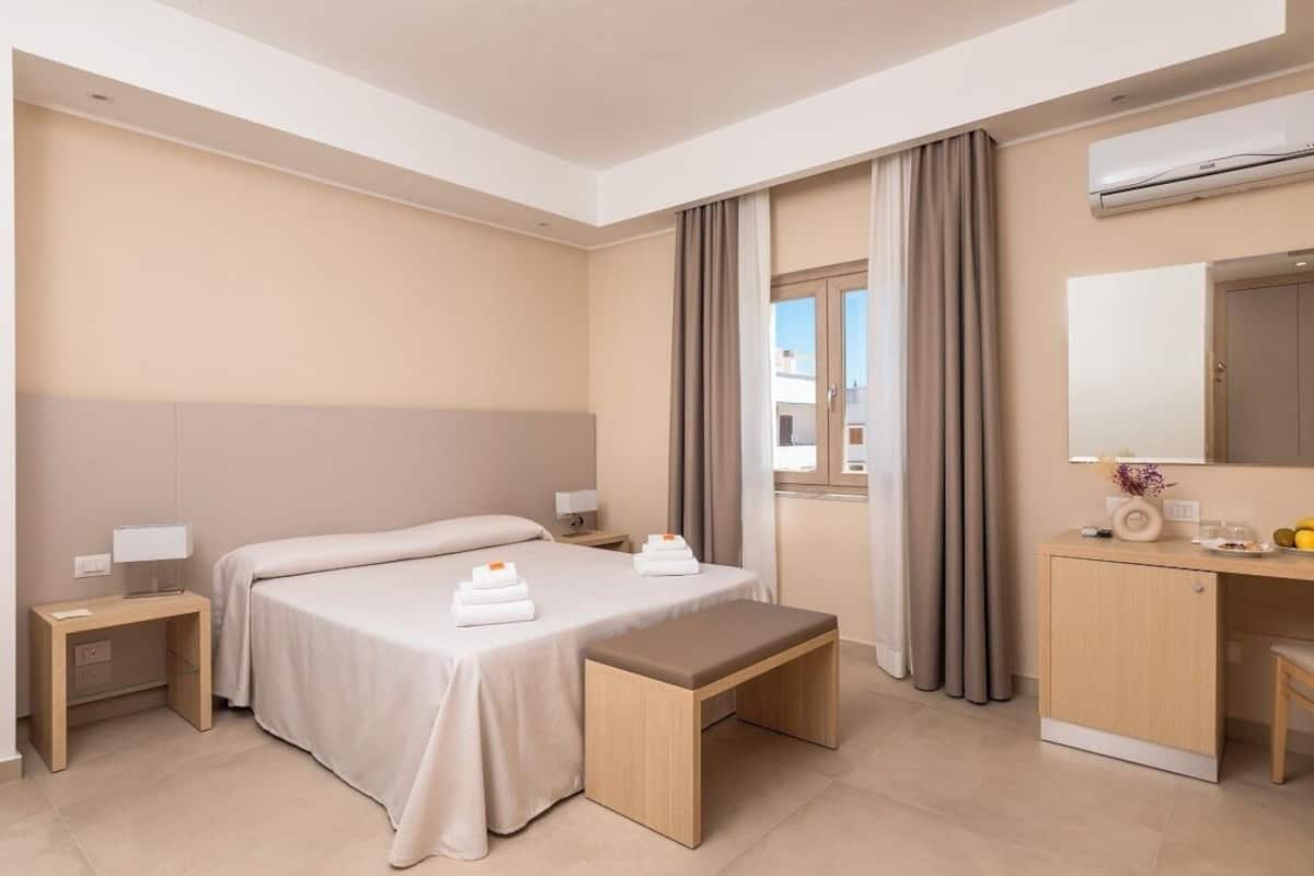 A hotel room with a bed, bedside tables, a desk, and a bench.