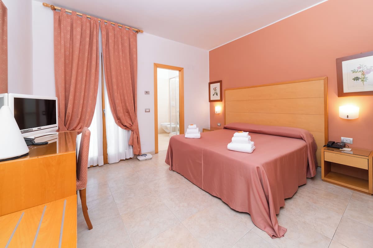 A hotel room with a bed, a desk with a computer, a telephone, and a nightstand with a lamp.