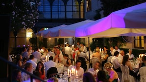 An outdoor dining area with tables set for guests, surrounded by a building with large windows and a covered section. - Relais Falisco (Civita Castellana)