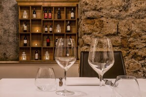 A table with three wine glasses and a bottle of wine, set against a stone wall with a wine rack in the background. - Relais Falisco (Civita Castellana)