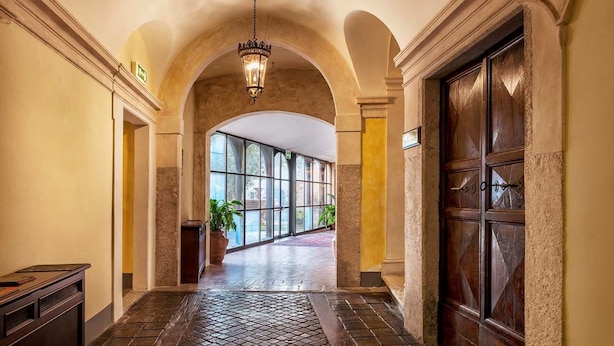 A hallway with a tiled floor, a wooden desk, a potted plant, and a large wooden door. - Relais Falisco (Civita Castellana)