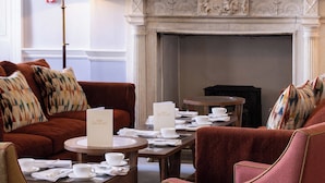 A room with a fireplace, a sofa, a table with cups and saucers, and a lamp. - Culloden House Hotel (Inverness)