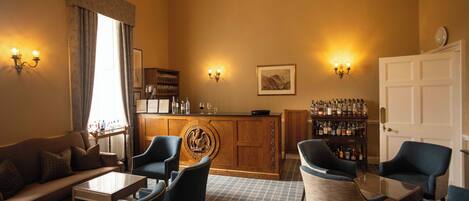A cozy lounge area with a sofa, armchairs, a coffee table, a bar area with a liquor display, and wall-mounted lighting.