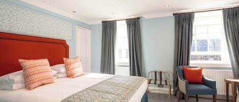 A hotel room with a large bed, a chair, a radiator, and a window with curtains.