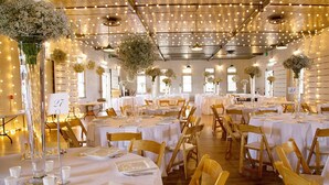 A banquet hall with round tables, white tablecloths, and wooden chairs. - Boothill Inn And Suites (Billings)