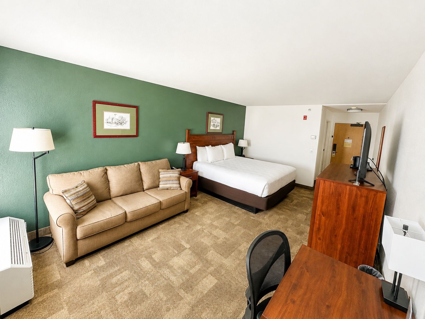 Quarto de hotel com cama, sofá, escrivaninha e cadeira.