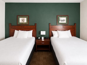 Una habitación de hotel con dos camas, una mesita de noche con lámpara y cuadros en la pared.