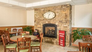 A dining area with round tables and chairs, a stone fireplace with a clock, and a patriotic sign. - Boothill Inn And Suites (Billings)