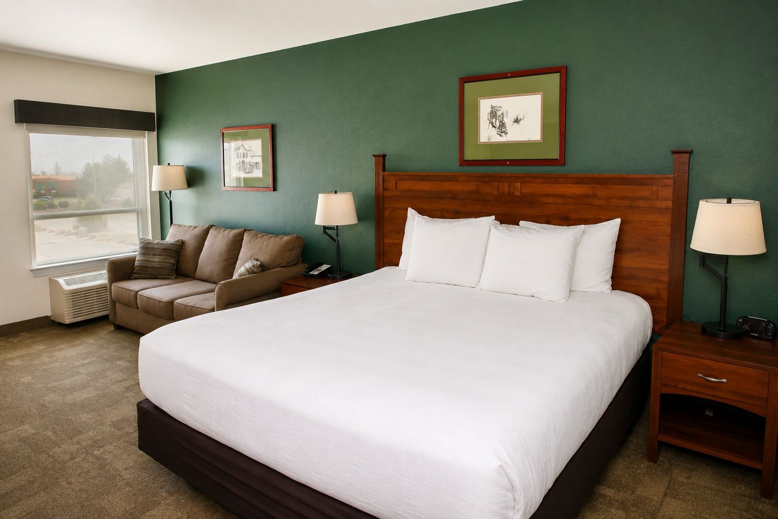 A hotel room with a large bed, two bedside tables, a nightstand, a window with blinds, a sofa, and two wall-mounted lamps.