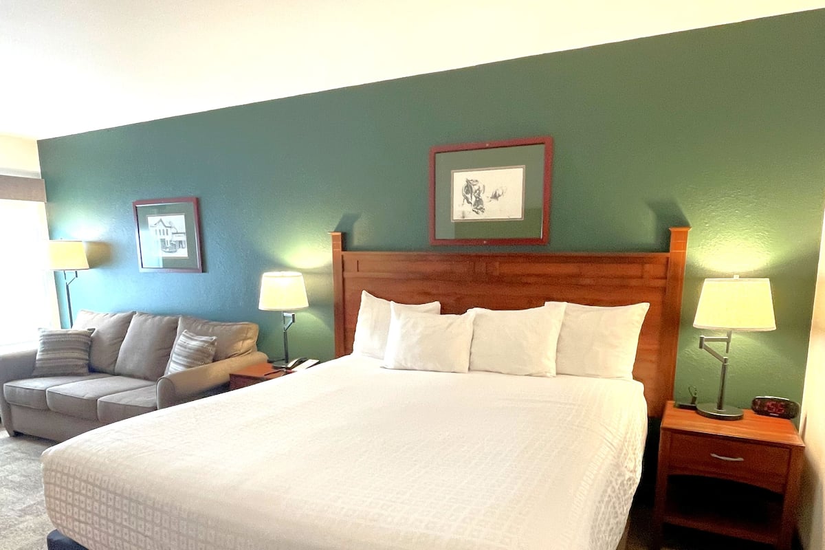 A hotel room with a large bed, two bedside tables, a nightstand, a sofa, and two wall-mounted lamps.