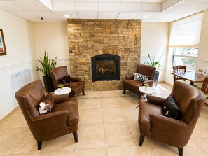 A room with a stone fireplace, leather armchairs, a dining table, and a large window.