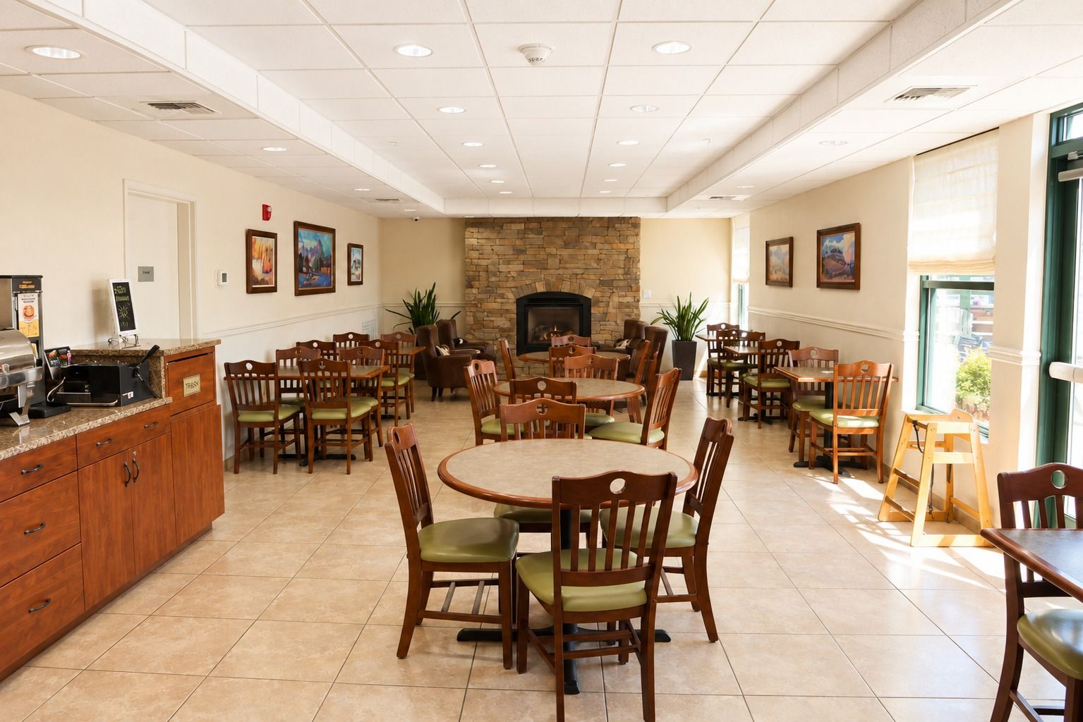 A spacious dining area with multiple tables and chairs, a stone fireplace, and a kitchen counter with a coffee machine.