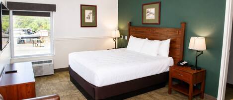 A hotel room with a large bed, a desk, a chair, a bedside table with a lamp, and two framed pictures on the wall.