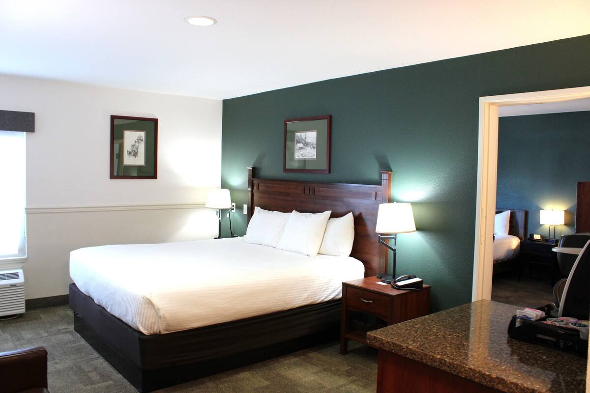 A hotel room with a large bed, bedside lamps, a desk with a telephone, and framed pictures on the wall.