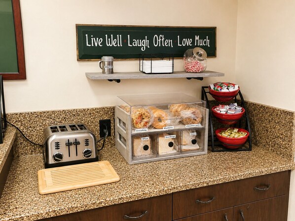 A kitchen counter with a toaster, a coffee maker, a sign saying 'Live Well Laugh Often Love Much,' and a container with labeled food items.