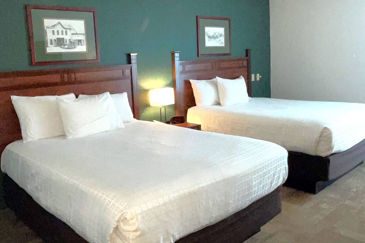 Two single beds with wooden headboards in a hotel room with green walls and framed pictures on the wall.