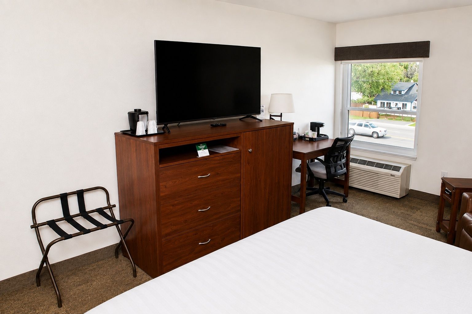 A hotel room with a bed, a desk, a television, a chair, and a window with a view of a street.