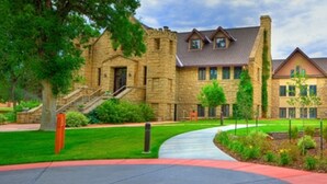 A stone building with a central tower, a covered walkway, and a well-maintained lawn. - Boothill Inn And Suites (Billings)