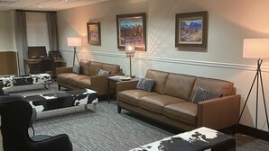 A hotel lobby with a seating area featuring a sofa, two armchairs, and a coffee table with a cowhide pattern. There are two lamps, a desk with a computer, and framed artwork on the walls. - Boothill Inn And Suites (Billings)