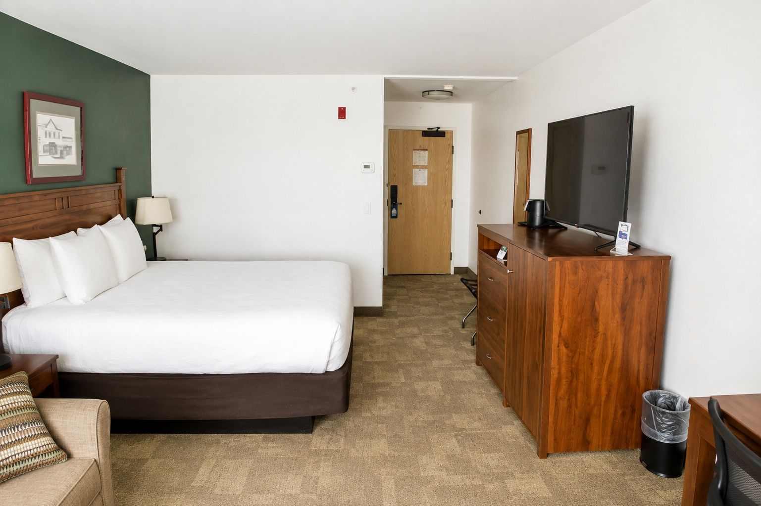 Une chambre d’hôtel avec un lit, une commode en bois, un téléviseur et une poubelle.