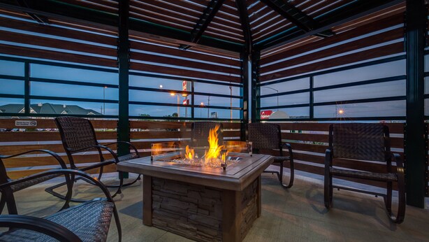 An outdoor patio with a stone fireplace, metal chairs, and a view of the city skyline at dusk. - Boothill Inn And Suites (Billings)