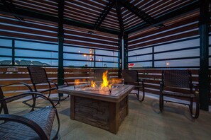 An outdoor patio with a stone fireplace, metal chairs, and a view of the city skyline at dusk. - Boothill Inn And Suites (Billings)